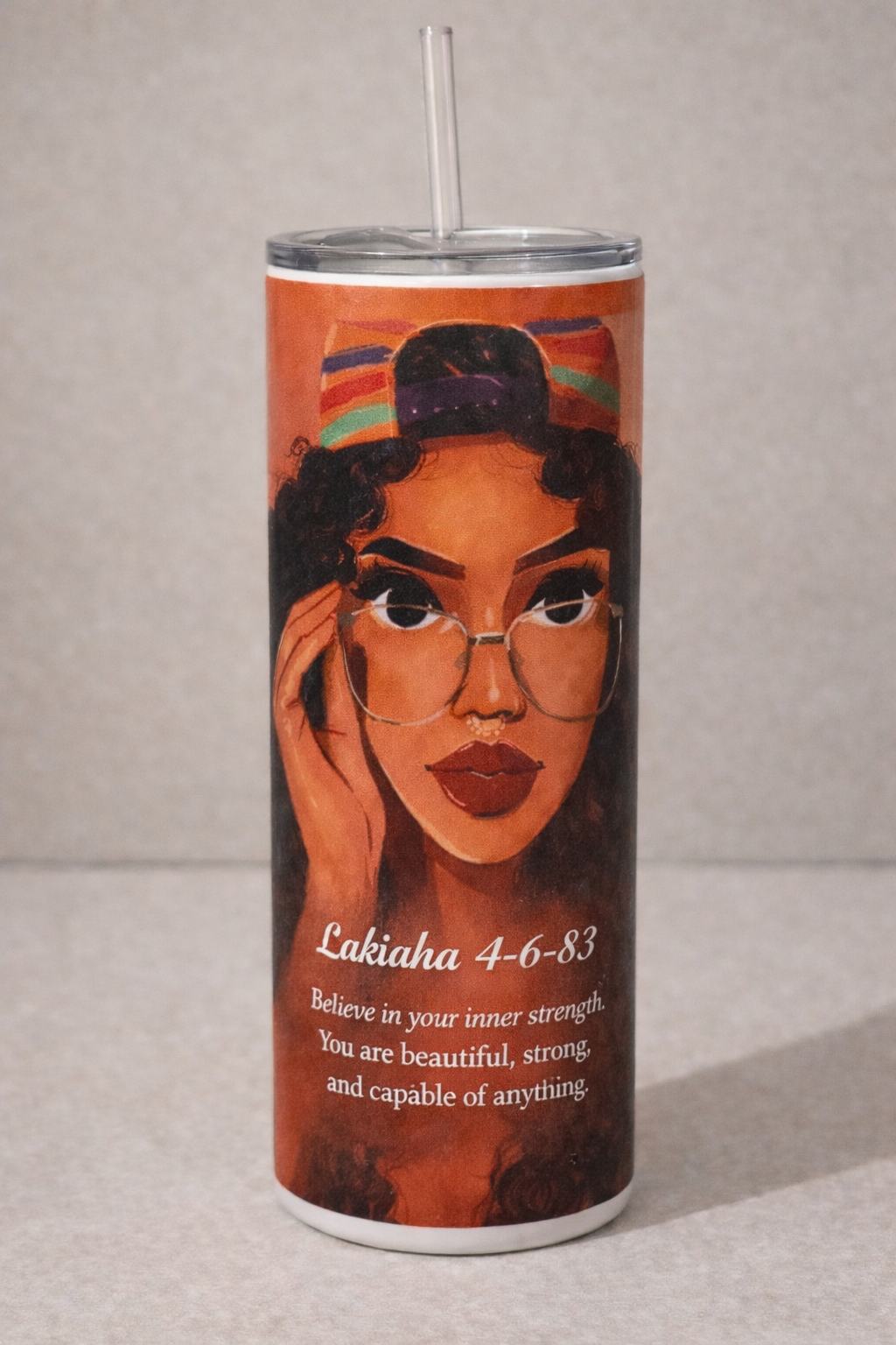 Tumbler with a design of a woman's face, text, and a colorful cap on a beige background